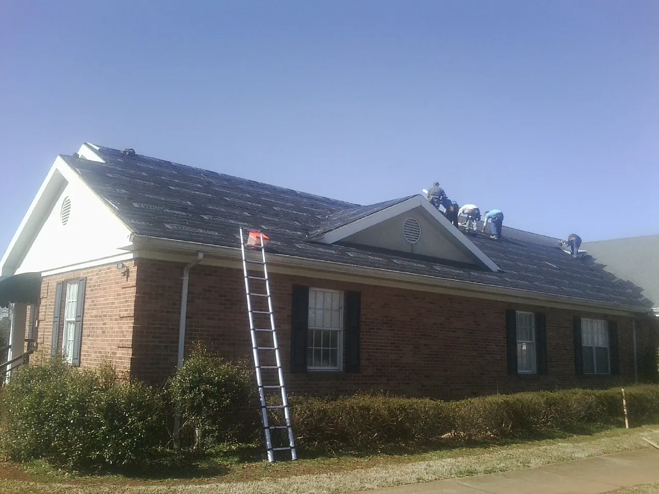 Crew tearing shingles off a brick ranch roof with a ladder set — Metal Roof Repair work by our crew in Monterey