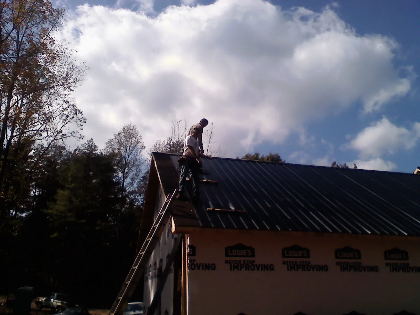 Roofer fastening dark metal panels high against a cloudy sky, from a Roof Inspection job in Monterey
